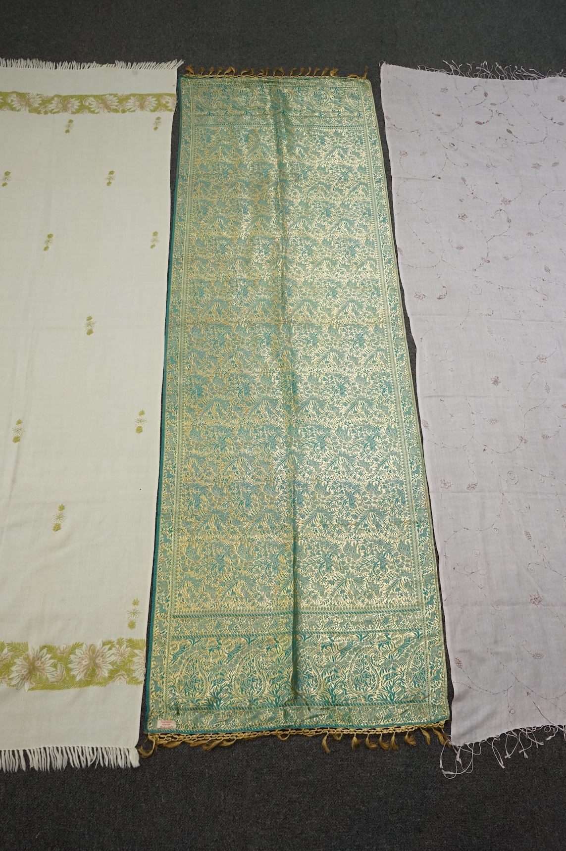 An Indian green and gold silk hand woven brocade stole, a cream pashmina embroidered stole and a similar finely woven and embroidered lilac stole (3). Brocade stole 38cm x 180cm., Condition - light stain to finely woven